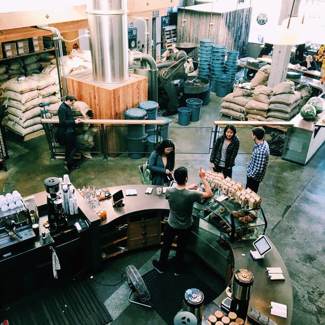 Showcasing modern coffee shop ambiance with customers and industrial coffee roasting equipment. Suitable for business marketing, cafe decor inspiration, urban lifestyle articles, and coffee culture promotions.