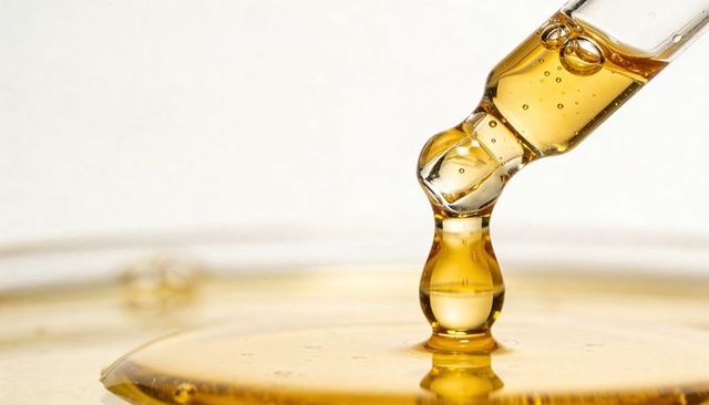 Golden serum droplet falling from glass pipette over viscous surface, bubbles and gloss