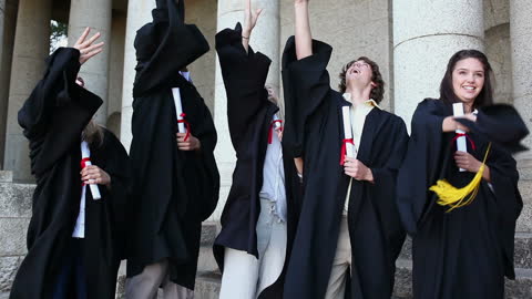 Excited Graduates Celebrating with Hat Toss in Front of University