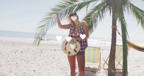 Woman enjoying tropical beach vacation wearing plaid shirt, bikini, shorts and sunglasses