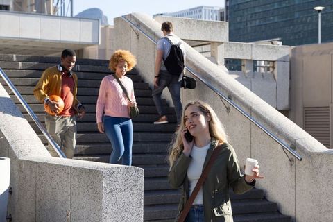 Diverse young adults descending concrete stairs in urban plaza, woman talking on phone