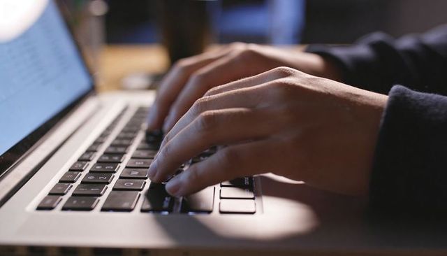 Closeup fingers typing on laptop keyboard at home office with warm evening glow