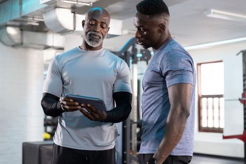 African american personal trainer reviewing workout plan with client on tablet in gym