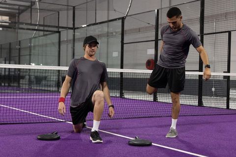 Stretching partners on purple padel court warming up before indoor training session