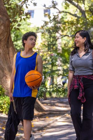 Teen basketball player walking with friend on park path holding ball and duffel