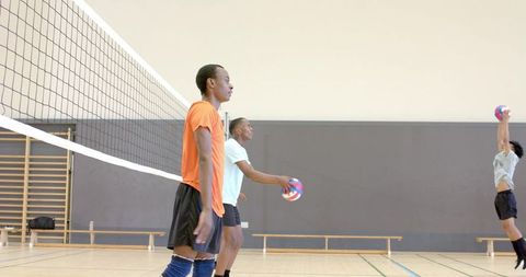 Diverse high school male teammates practicing volleyball drill near net in indoor gym