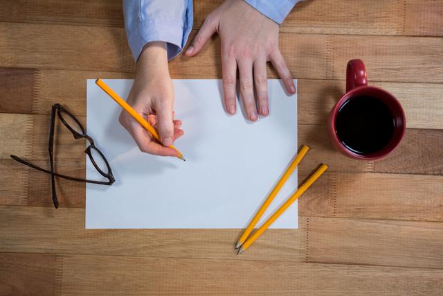 Businesswoman writing on a blank sheet of paper at a wooden desk with coffee, pencils, and glasses. Ideal for illustrating concepts of planning, creativity, organization, and professional work environments.