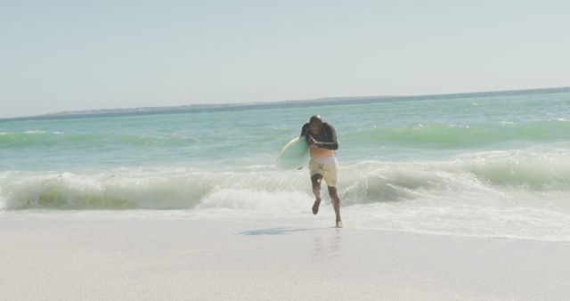 Man running along beach with surfboard on sunny day - Download Free Stock Images Pikwizard.com