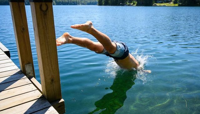 Man diving headfirst from wooden dock into clear lake on sunny summer day splash action