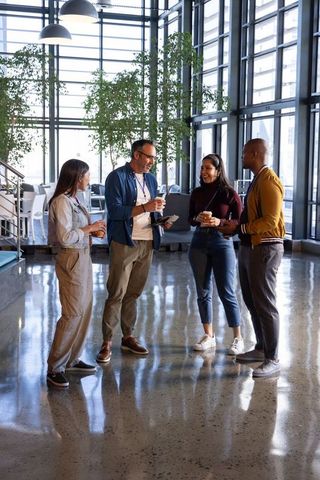 Diverse coworkers collaborating in modern office atrium during informal coffee break