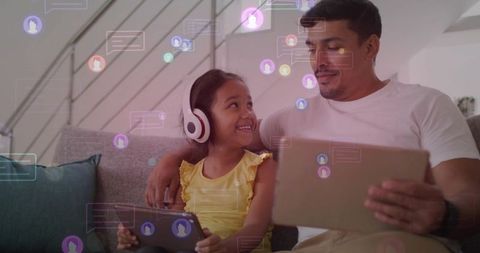 Father and daughter sharing tablets on couch, bonding through digital learning