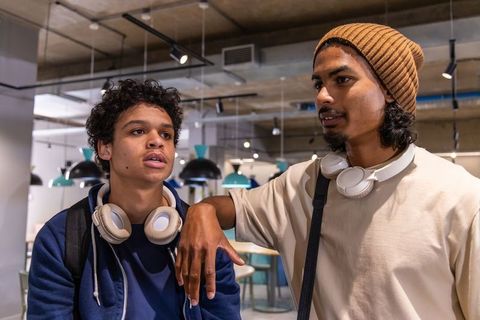 Teen friends collaborating in modern cafe with headphones and backpacks