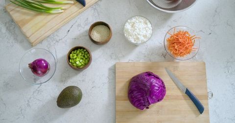 Overhead food prep with halved purple cabbage, avocado and fresh salad ingredients