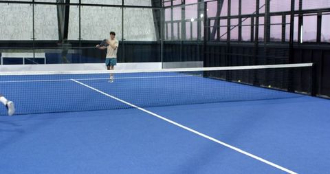 Male athletes playing padel behind glass barriers on blue court