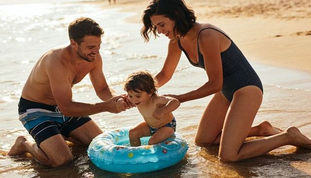 Parents guiding toddler into inflatable ring on sunlit beach during golden hour bonding