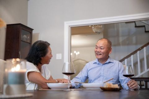 Senior asian mother and adult son sharing cozy candlelit dinner with wine, home togetherness
