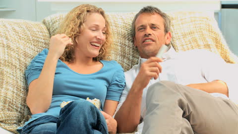 Smiling Couple Relaxing on Couch Enjoying Movie Time Together