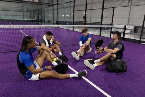Padel players sitting on purple court relaxing and discussing strategy after practice with rackets