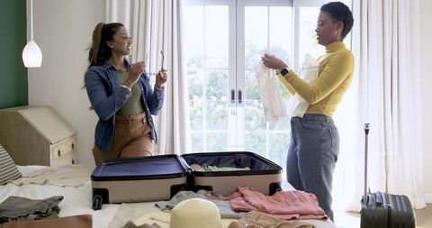 Diverse Female Friends Packing for Travel in Light-Filled Bedroom