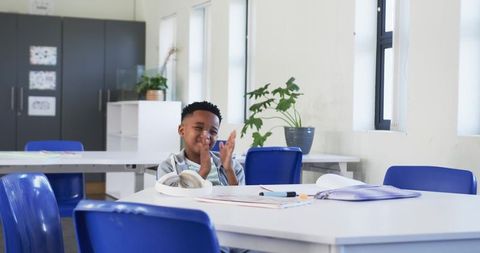 Joyful african american boy clapping during solo study session in bright modern classroom