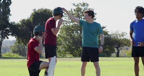 Cricket teammates adjusting helmet during outdoor training on grass field promoting safety
