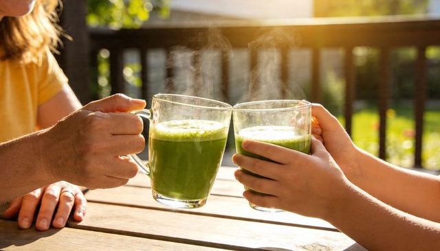 Grandparent and child toasting steaming green smoothies on sunlit wooden patio