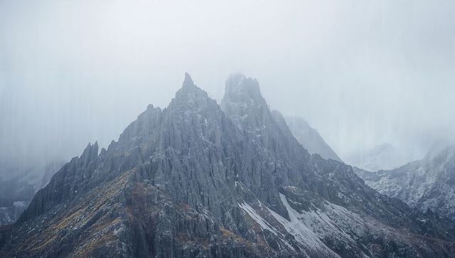 Rising jagged mountain ridge climbing into low cloud with snow-patched spires, moody fog