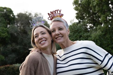 Mother and daughter wearing merry christmas headbands smiling together in park casual sweaters