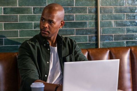 African man working on laptop in cozy cafe booth with coffee and green tile wall