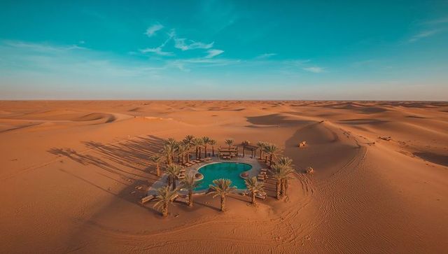 Desert oasis featuring turquoise kidney-shaped pool and palm trees amid rolling sand dunes