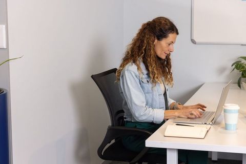 Mature professional woman typing on laptop at minimalist desk with notebook and coffee