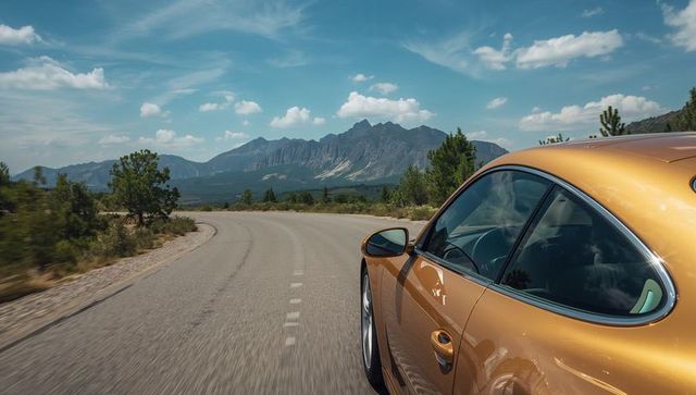 Gold sports car cruising along winding mountain highway with dramatic clouds and reflections