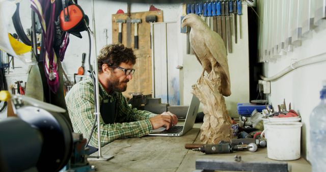 Craftsman Working on Laptop in Workshop with Large Bird Sculpture - Download Free Stock Images Pikwizard.com