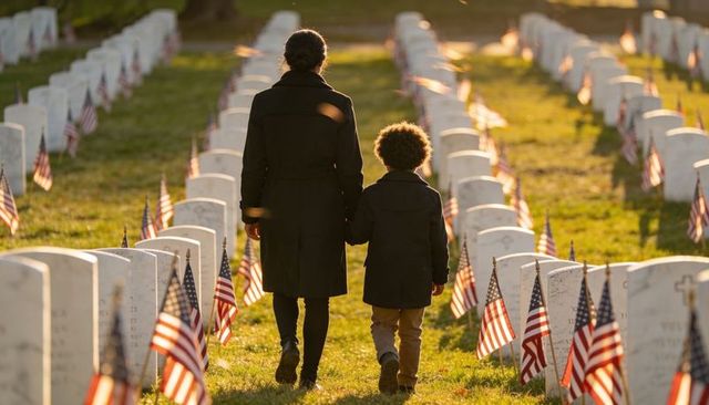 Parent and child walking through military cemetery lined with american flags at sunset