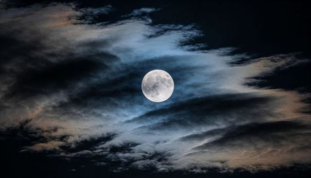 Full Moon Revealing Crater Detail Amid Wispy Layered Clouds in Night Sky