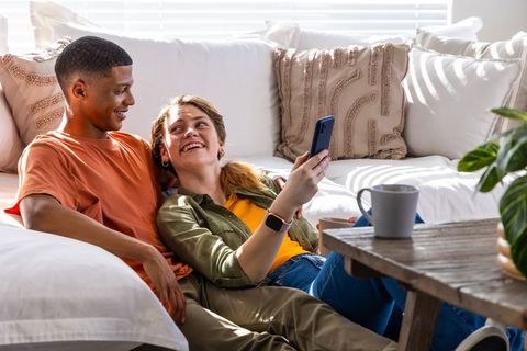 Couple relaxing on white sofa sharing smartphone and laughing together