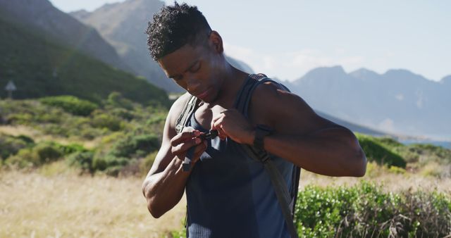 African american man exercising outdoors putting backpack on in countryside on a mountain. fitness training and healthy outdoor lifestyle.