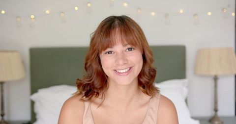 Smiling Young Woman in Cozy Bedroom with Warm Ambiance