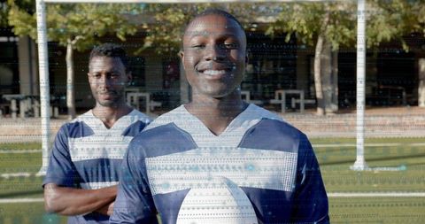 Smiling male football player holding ball with teammate on sunny grass field showing teamwork