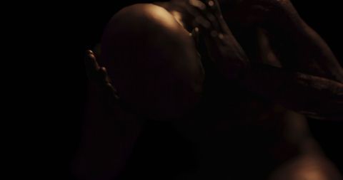 Distressed bald figure holding head in darkness