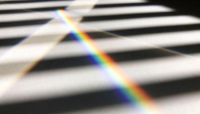 Diagonal rainbow band crossing blinds shadows abstract prism light spectrum background