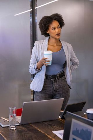 Confident Entrepreneur Enjoying Coffee and Standing in Modern Office