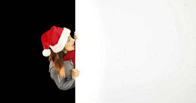 Woman wearing Santa hat and red scarf peeking from behind a blank panel. Suitable for holiday-themed promotions, greeting cards, event invitations, and festive advertisements.