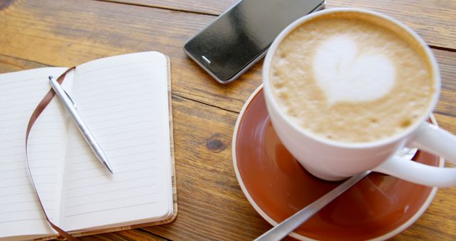 A cup of coffee sits next to a notebook and phone on a wooden table. The scene captures a cozy coffee break ideal for planning or reflection.