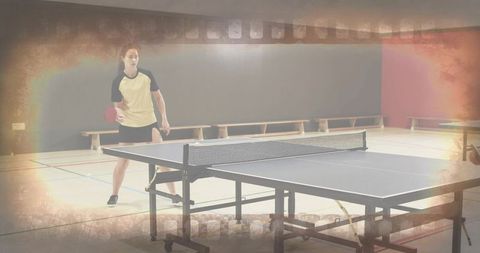 Woman playing table tennis in gymnasium preparing for serve during indoor training session