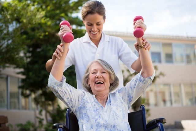 Female doctor assisting senior woman in wheelchair with lifting dumbbells in a park. Ideal for use in healthcare, elderly care, physical therapy, and active lifestyle promotions. Highlights the importance of fitness and rehabilitation for seniors.