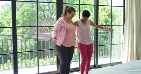 Diverse women practicing balance on bed near sliding glass doors morning fitness