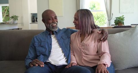 Senior couple sharing warm embrace on couch in bright living room, casual home lifestyle