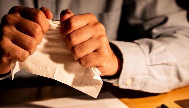 Tearing tissue in frustration closeup hands gripping paper over desk with documents