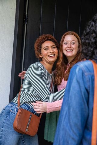 Diverse Female Friends Hugging Visitor at Home Entrance